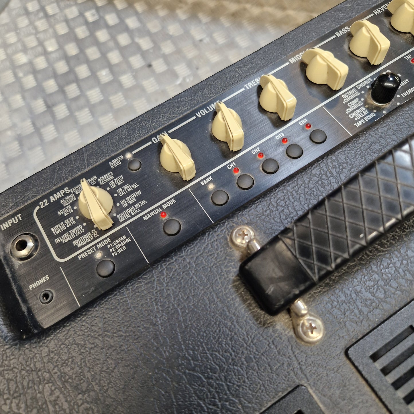 Pre-Owned Vox VT100 Valvetronix 100w Electric Combo Close-up of a black guitar amplifier control panel with cream-colored knobs, red indicator lights, and a black textured body, photographed on a metal floor.