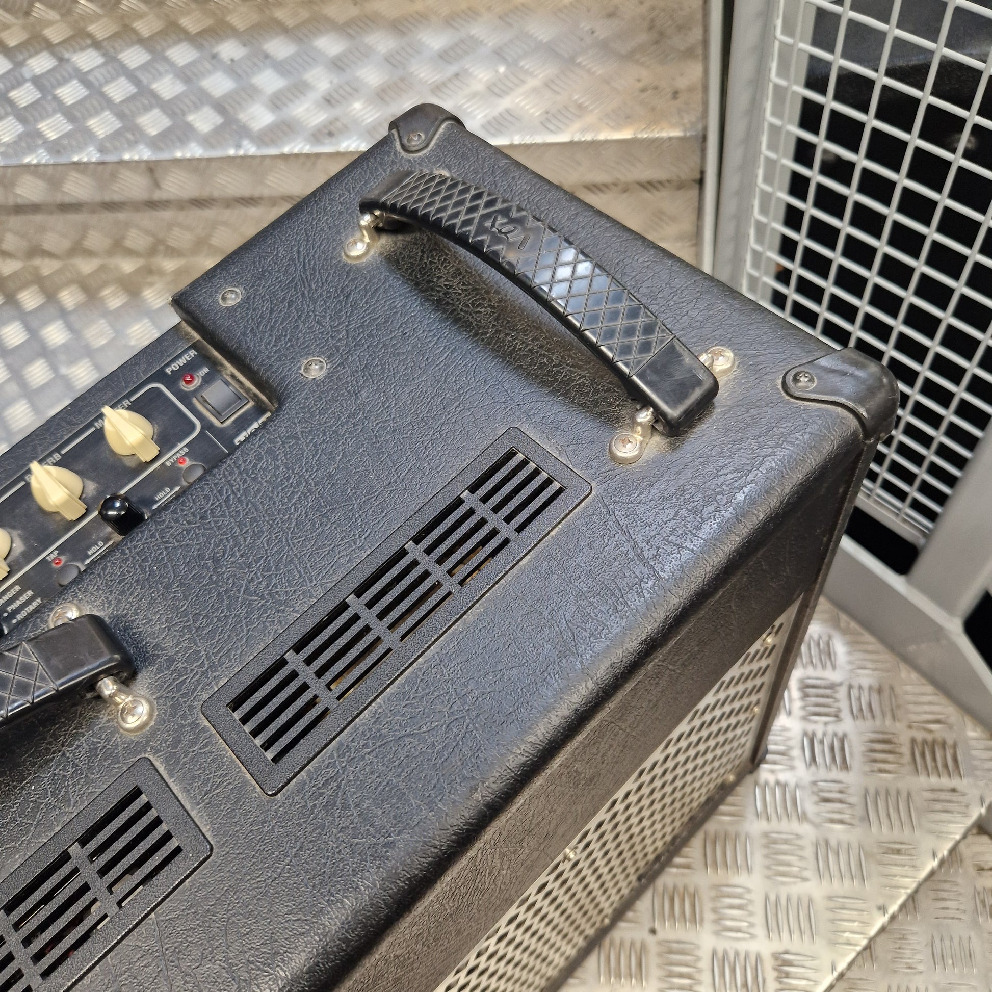 Pre-Owned Vox VT100 Valvetronix 100w Electric Combo Close-up of the top and side of a black textured guitar amplifier head with control knobs, vent grilles, and a handle, photographed on a metal diamond-plate floor.
