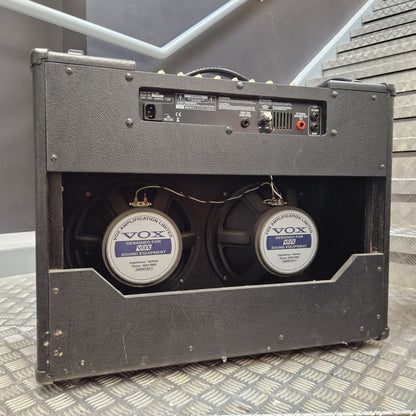Pre-Owned Vox VT100 Valvetronix 100w Electric Combo A black Vox double speaker guitar amplifier shown from the rear, featuring two large speakers with Vox Registration 8000 labels, set against a gray staircase background.