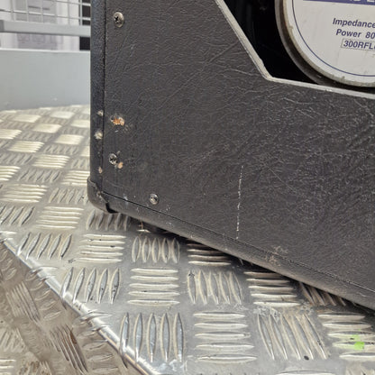 Pre-Owned Vox VT100 Valvetronix 100w Electric Combo Close-up of the corner of a black textured equipment cabinet or speaker housing resting on a diamond plate metal surface.