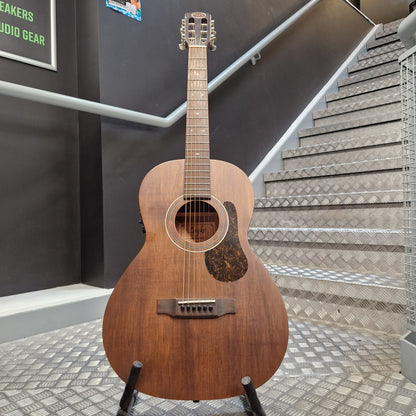 Pre-Owned Layke Smokestack Parlour Electro-Acoustic - Mahogany A vintage acoustic guitar with a medium brown wooden body and a dark tortoiseshell pickguard, displayed on a stand in front of a staircase.