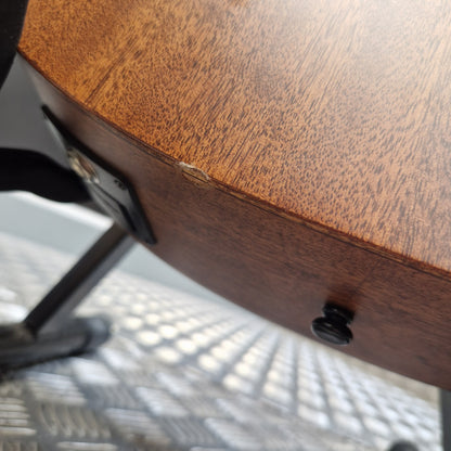 Pre-Owned Layke Smokestack Parlour Electro-Acoustic - Mahogany Close-up of the underside of a wooden chair, showing a medium brown wood grain finish, a black metal support bracket, and a black leg knob, with a metal mesh chair base visible underneath.