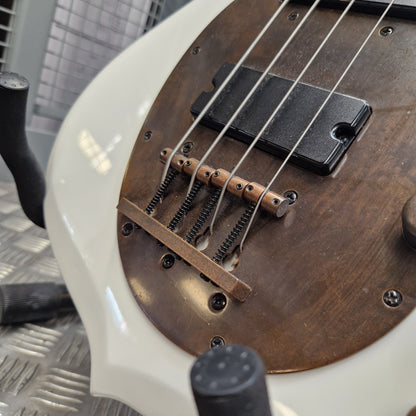 Pre-Owned Traben Neo 4 Bass - White Close-up of a bass guitar body showing a white outer shell, a brown wood pickguard, four metal strings, and a black pickup on a metal floor.