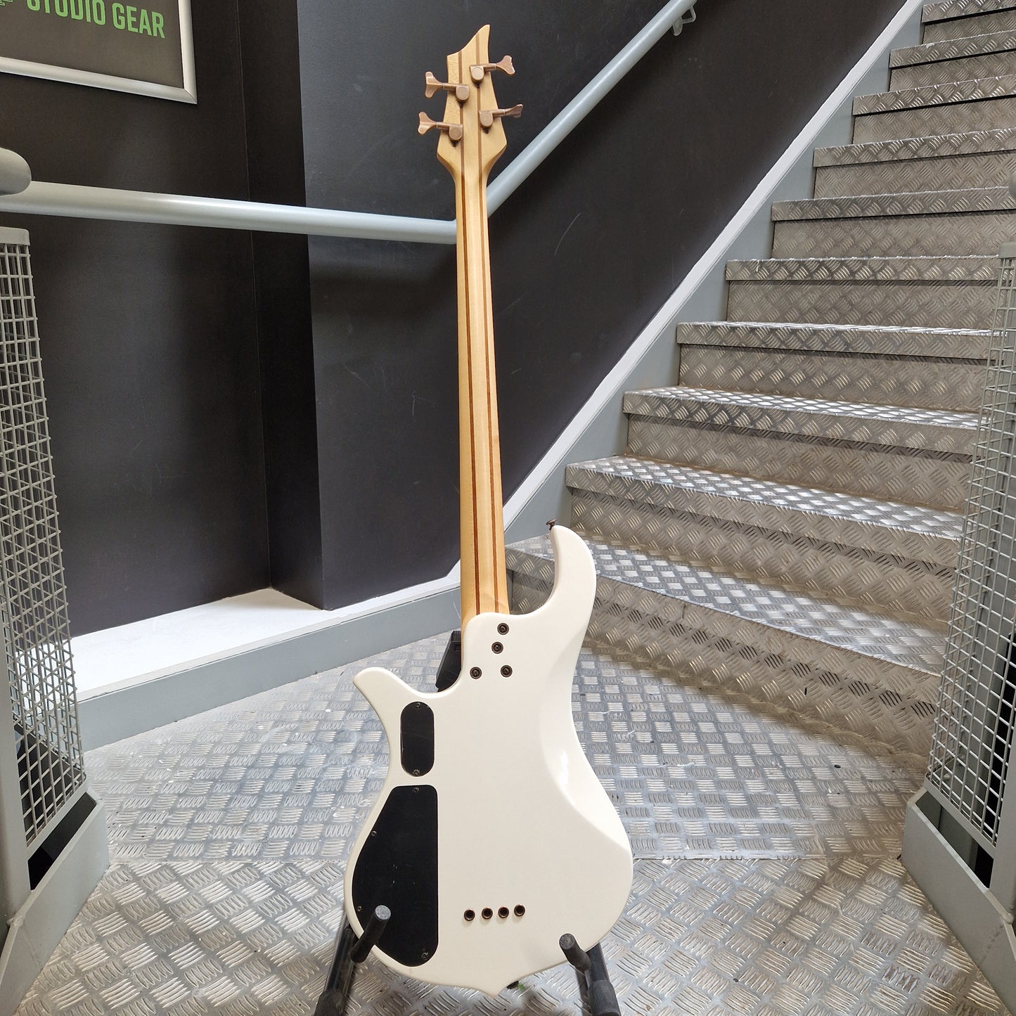 Pre-Owned Traben Neo 4 Bass - White A white electric bass guitar with a natural wood neck and black pickguard, standing on a stand in front of an indoor staircase.
