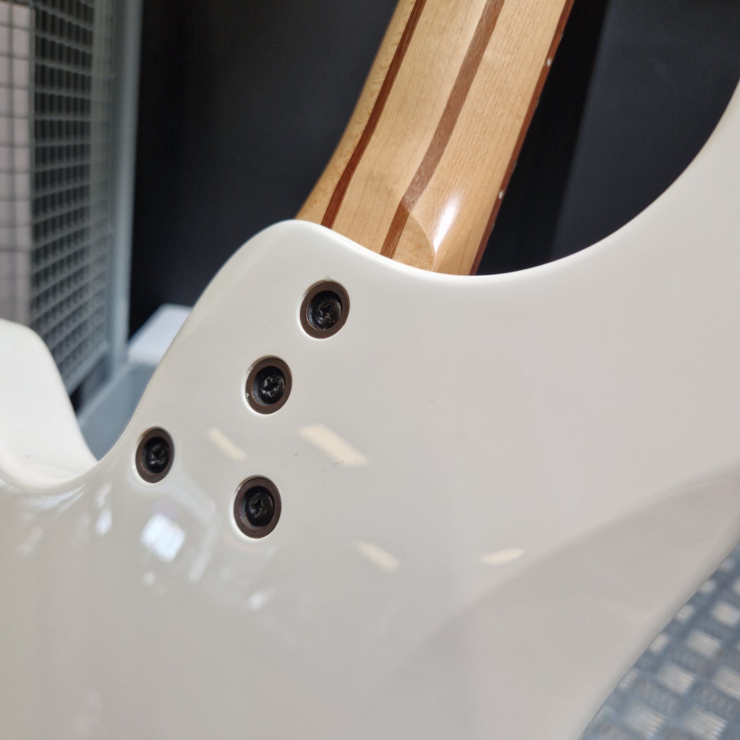 Pre-Owned Traben Neo 4 Bass - White Close-up of the lower bout body of a white electric guitar, showing four black control screws and part of the natural wood neck with dark stripes.