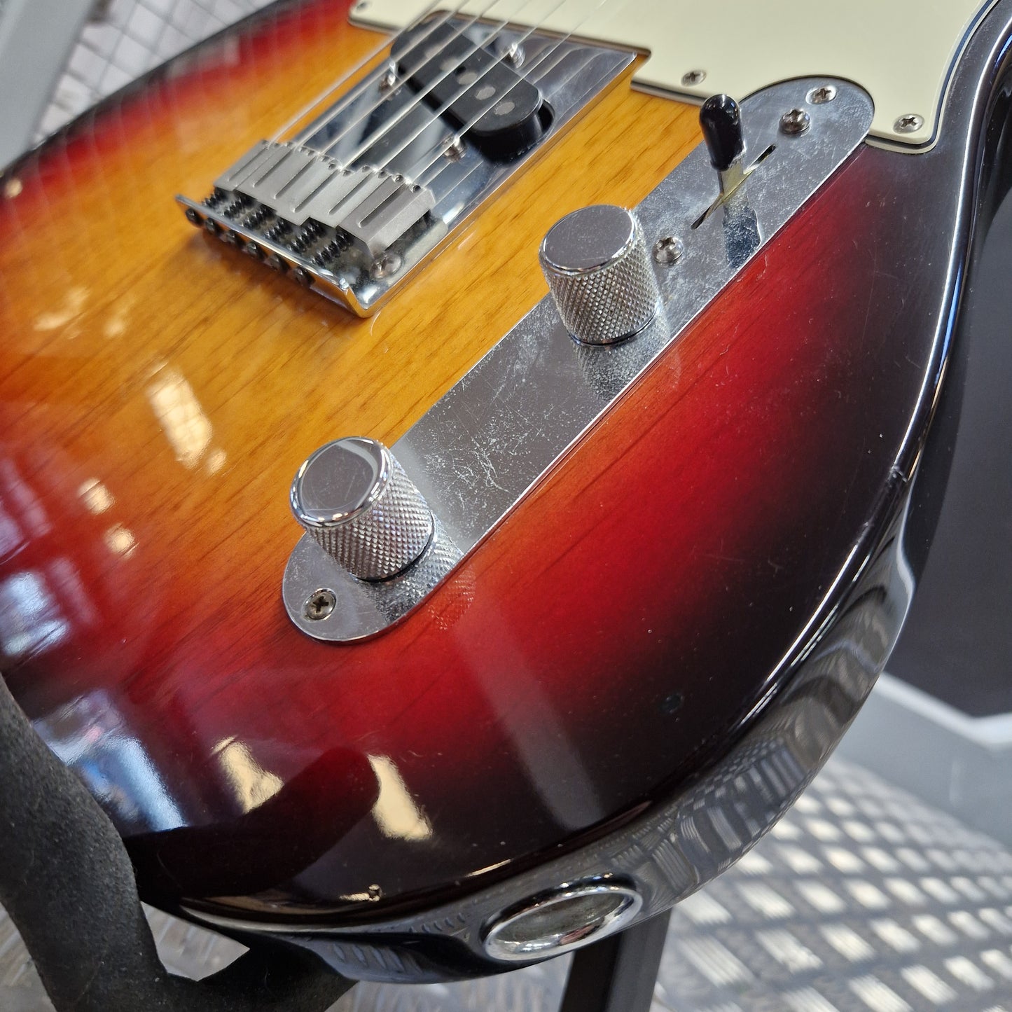 Pre-Owned Fender American Standard Telecaster 2000 Electric - 3-Colour Sunburst Close-up of the lower body of a sunburst electric guitar, showing the glossy red-to-brown gradient finish, chrome hardware, and control knobs.