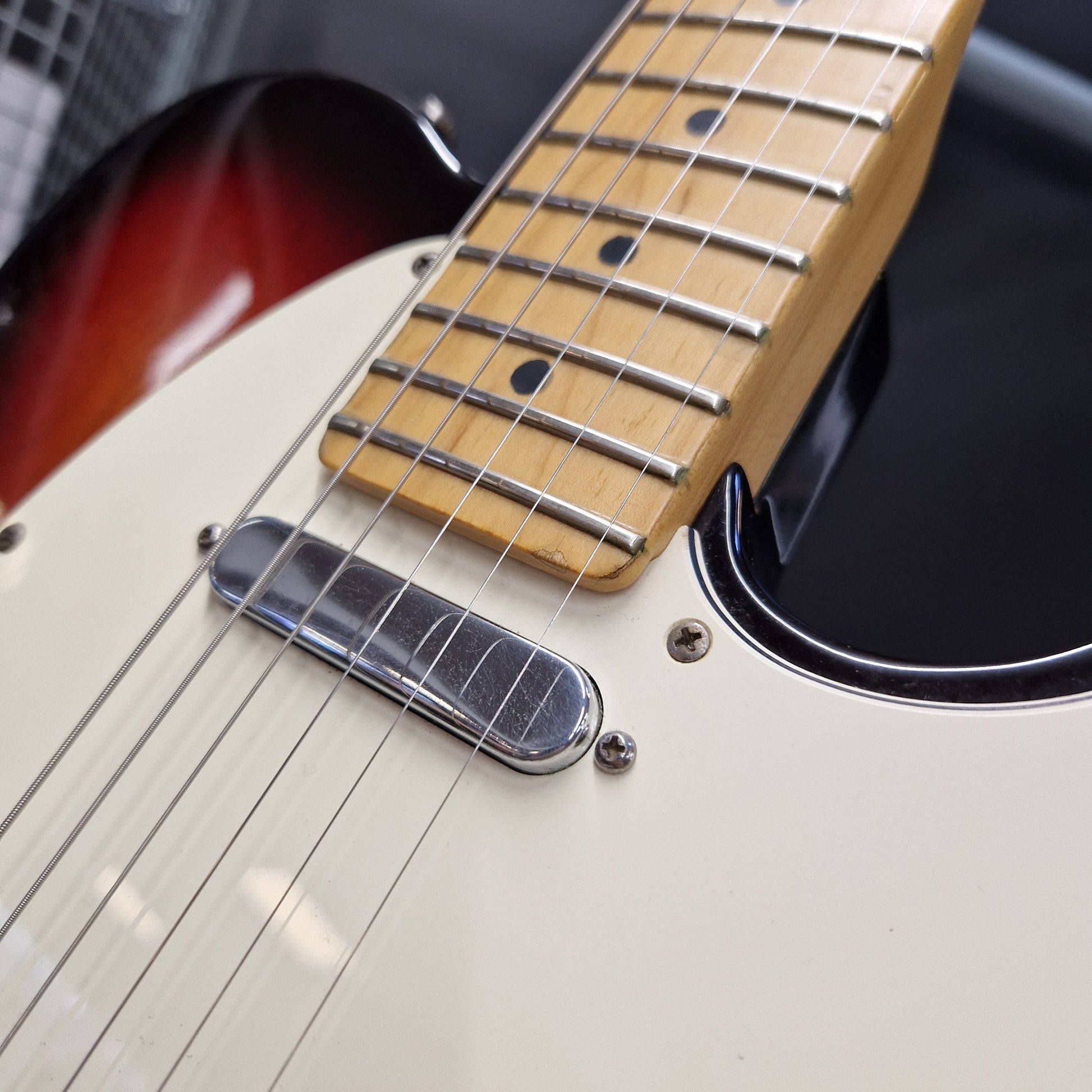 Pre-Owned Fender American Standard Telecaster 2000 Electric - 3-Colour Sunburst Close-up of a guitar body and neck showing a cream-colored pickguard, maple fretboard, and part of a sunburst finish on the upper bout.