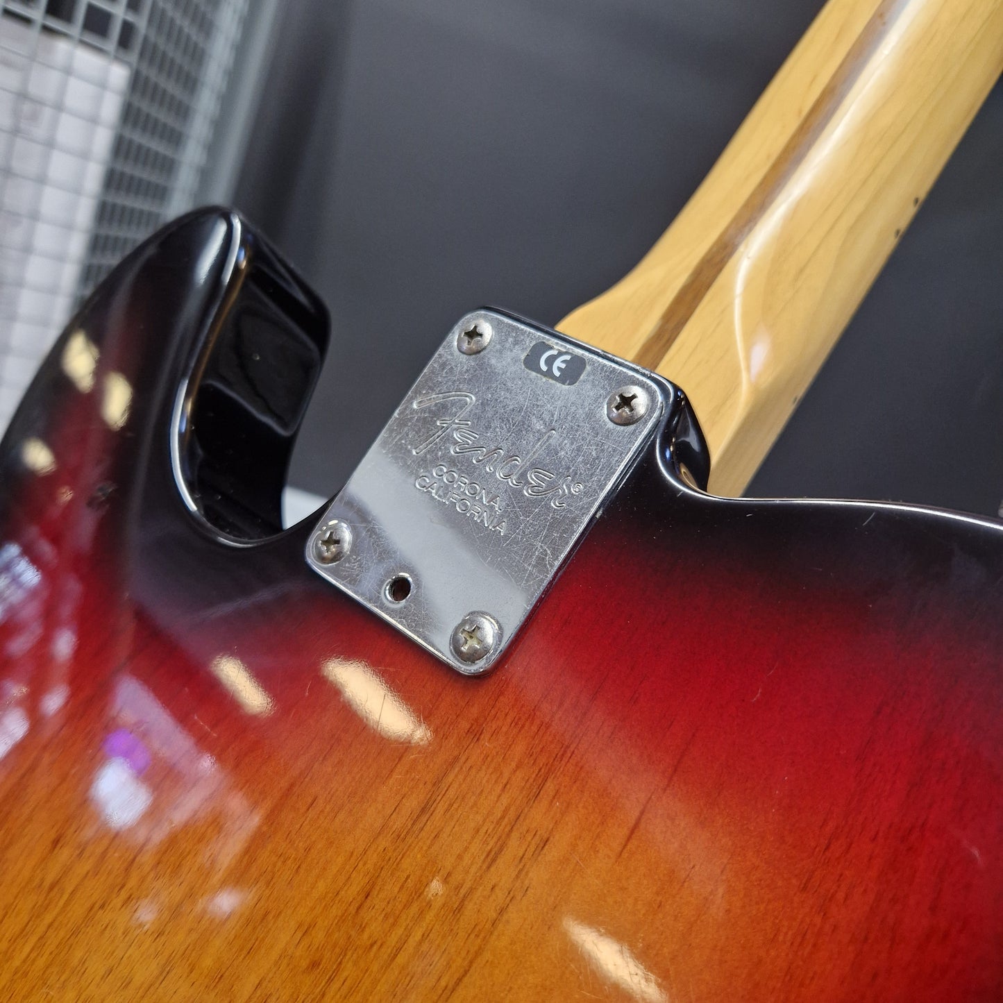 Pre-Owned Fender American Standard Telecaster 2000 Electric - 3-Colour Sunburst Close-up of a Fender electric guitar body showing the silver metal tailpiece plate with screws, a glossy red-to-brown sunburst finish, and part of the natural wood neck.