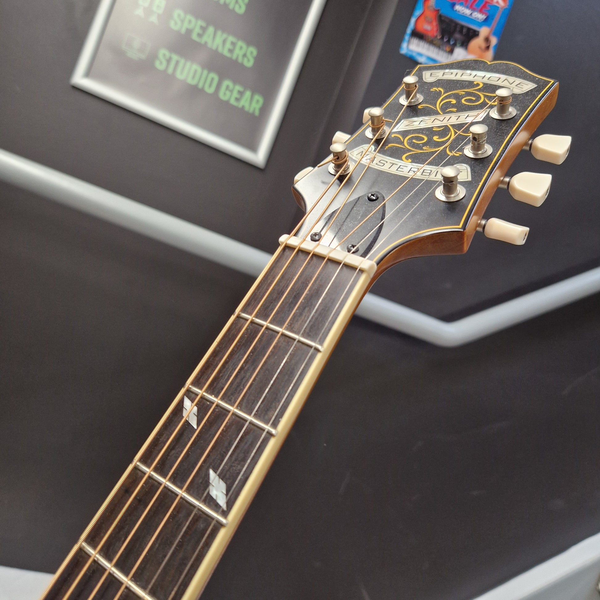 Pre-Owned Epiphone Masterbilt Zenith Classic Electro-Acoustic - Vintage Natural Close-up of a Fender Jazzmaster electric guitar headstock and neck, showing the gold-toned tuners, decorative headstock graphics, and dark fretboard against a dark display background.