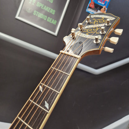 Pre-Owned Epiphone Masterbilt Zenith Classic Electro-Acoustic - Vintage Natural Close-up of a Fender Jazzmaster electric guitar headstock and neck, showing the gold-toned tuners, decorative headstock graphics, and dark fretboard against a dark display background.