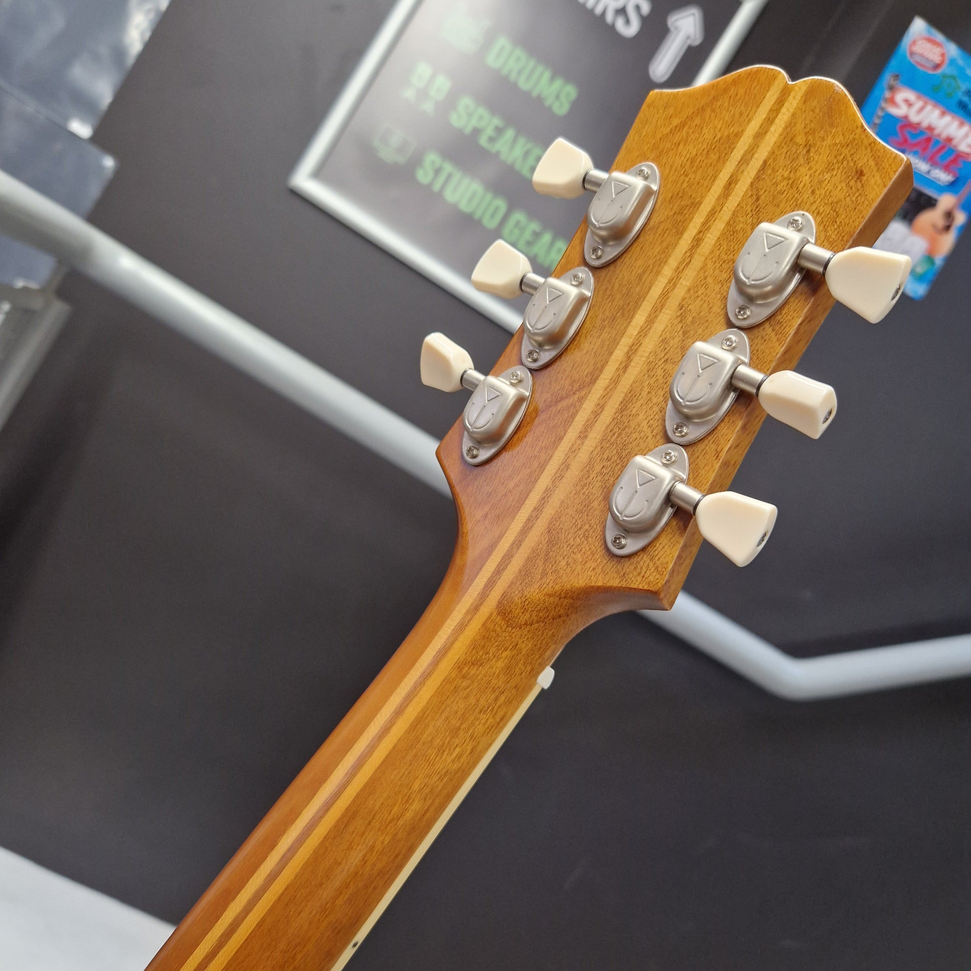 Pre-Owned Epiphone Masterbilt Zenith Classic Electro-Acoustic - Vintage Natural Close-up of the headstock of an acoustic guitar, showing six tuning pegs and a warm wood finish, with a blurred studio background.