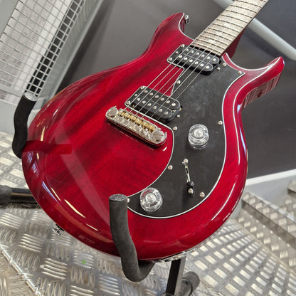 Pre-Owned PRS SE S2 Mira Electric - Wine Red A red electric guitar with a glossy cherry red finish, black pickguard, and chrome hardware, resting on a black guitar stand on a metal diamond plate floor.