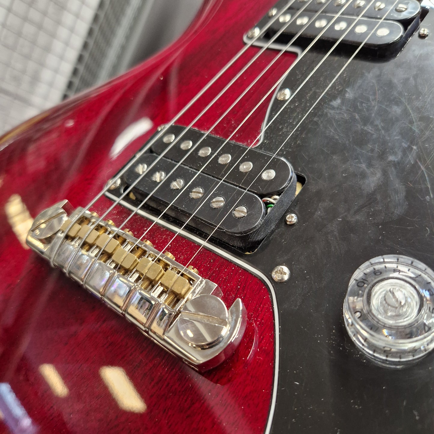 Pre-Owned PRS SE S2 Mira Electric - Wine Red Close-up of a red electric guitar body showing the bridge, pickups, strings, and control knob against a dark black pickguard.