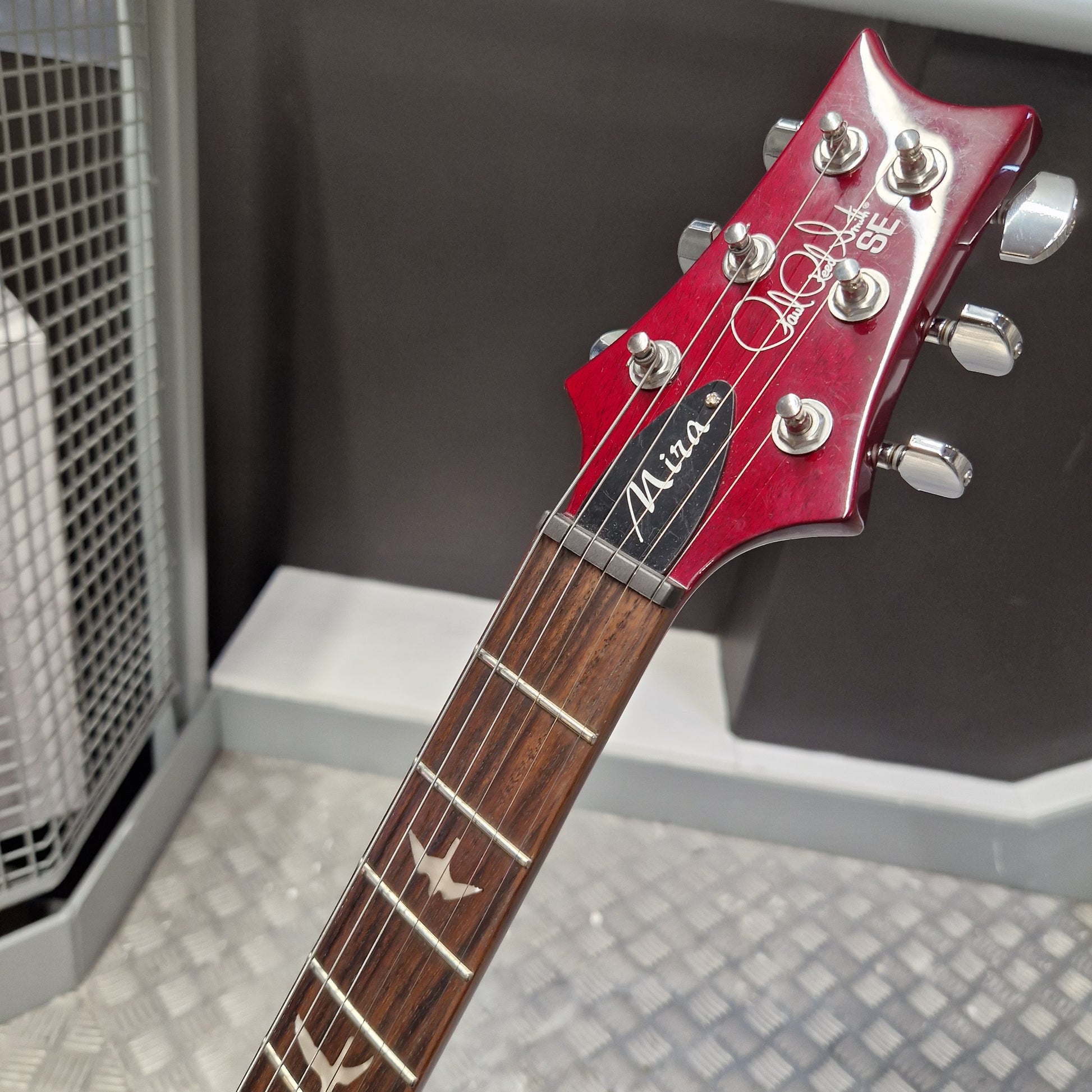 Pre-Owned PRS SE S2 Mira Electric - Wine Red Close-up of a red Gibson Les Paul Custom 'Mara' electric guitar headstock and neck, showing the silver tuning pegs and dark wood fretboard in an indoor setting.