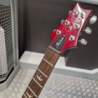 Pre-Owned PRS SE S2 Mira Electric - Wine Red Close-up of a red Gibson Les Paul Custom 'Mara' electric guitar headstock and neck, showing the silver tuning pegs and dark wood fretboard in an indoor setting.