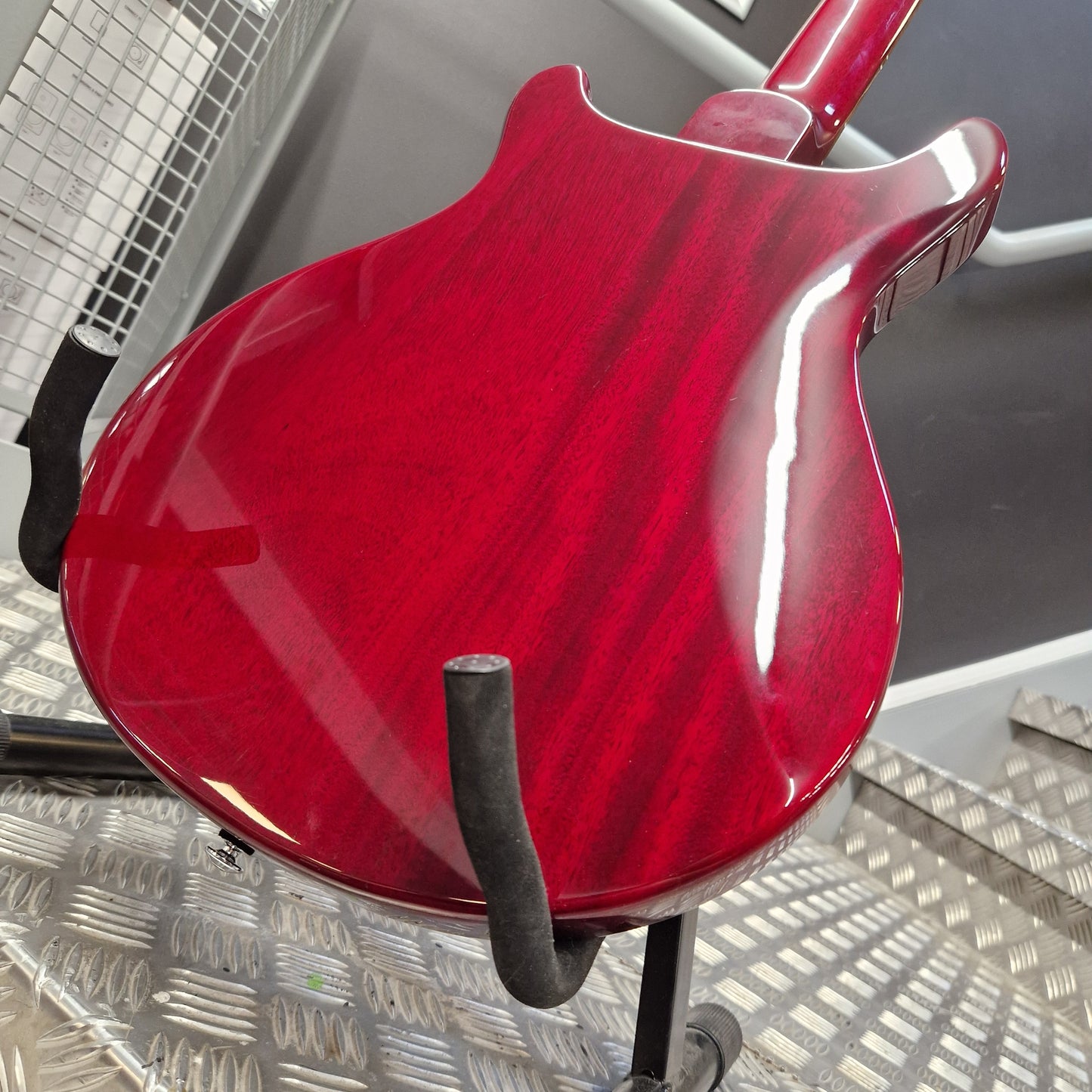 Pre-Owned PRS SE S2 Mira Electric - Wine Red Close-up of the glossy back of an electric guitar body in a deep red finish, resting on a black stand on a metal diamond plate floor.