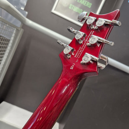 Pre-Owned PRS SE S2 Mira Electric - Wine Red Close-up of the headstock of a glossy red electric guitar, showing six silver tuning pegs and printed model text on the back of the neck, set against a dark gray indoor background.