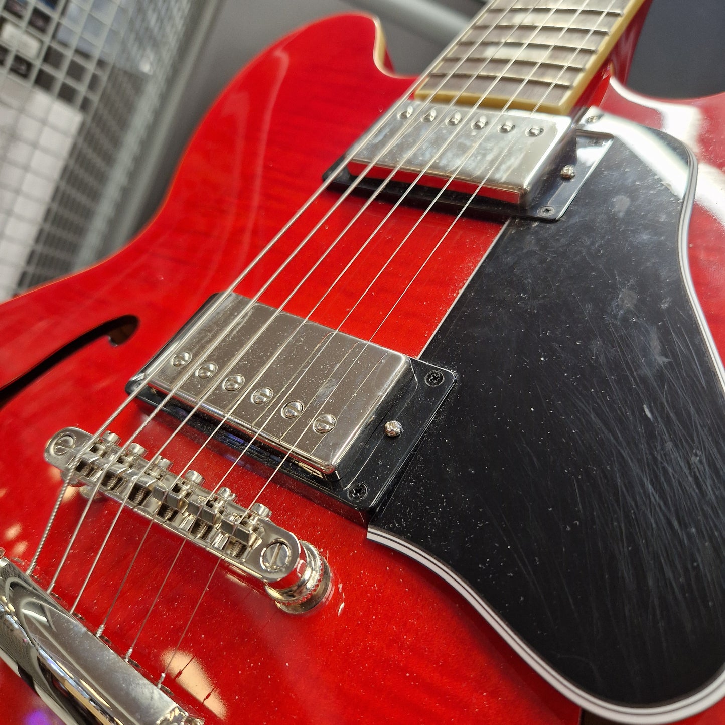 Pre-Owned Epiphone ES-335 Figured Semi-Hollow Electric - Sixties Cherry Close-up of a red electric guitar body with a black pickguard, chrome hardware, and part of the fretboard visible.