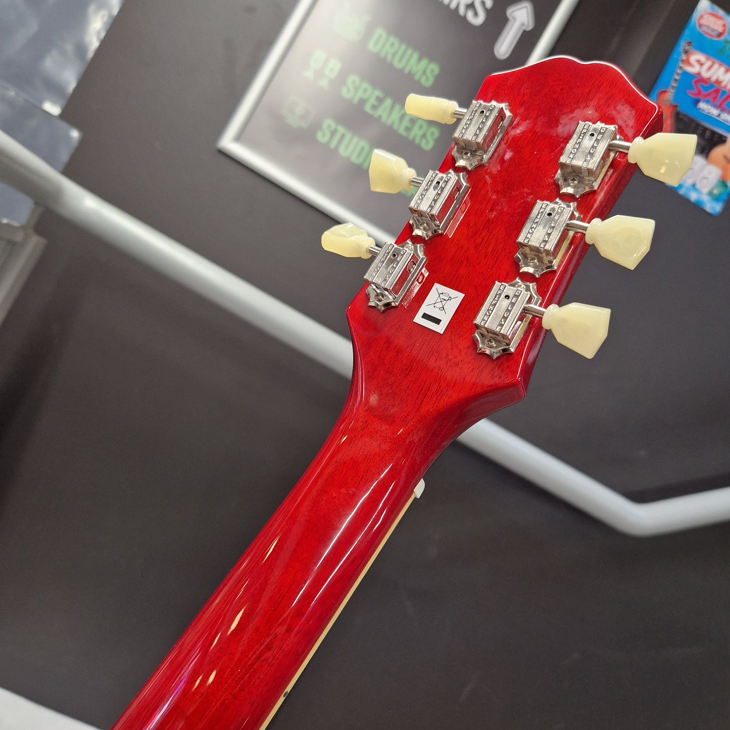 Pre-Owned Epiphone ES-335 Figured Semi-Hollow Electric - Sixties Cherry Close-up of the headstock of a glossy red electric guitar, showing six silver tuning pegs with cream-colored knobs, photographed in a store setting.