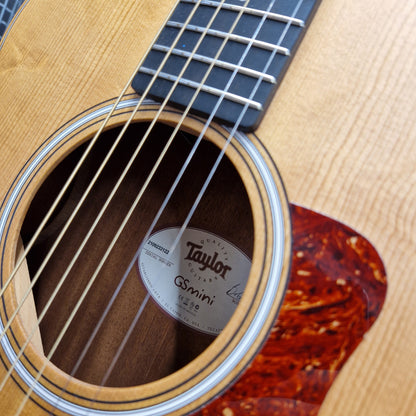 Pre-Owned Taylor GS Mini-e Electro-Acoustic - Limited Edition Quilted Sapele Close-up of an acoustic guitar body showing the sound hole, strings, wood grain, and a Taylor Gsinini label.