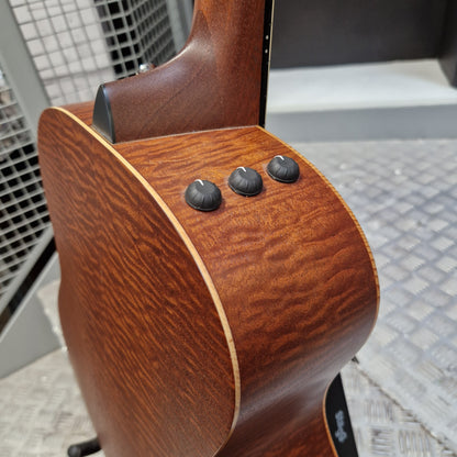 Pre-Owned Taylor GS Mini-e Electro-Acoustic - Limited Edition Quilted Sapele Close-up of the back of an acoustic guitar showing the rich wood grain finish, three black control knobs, and the edge of the soundhole cover.