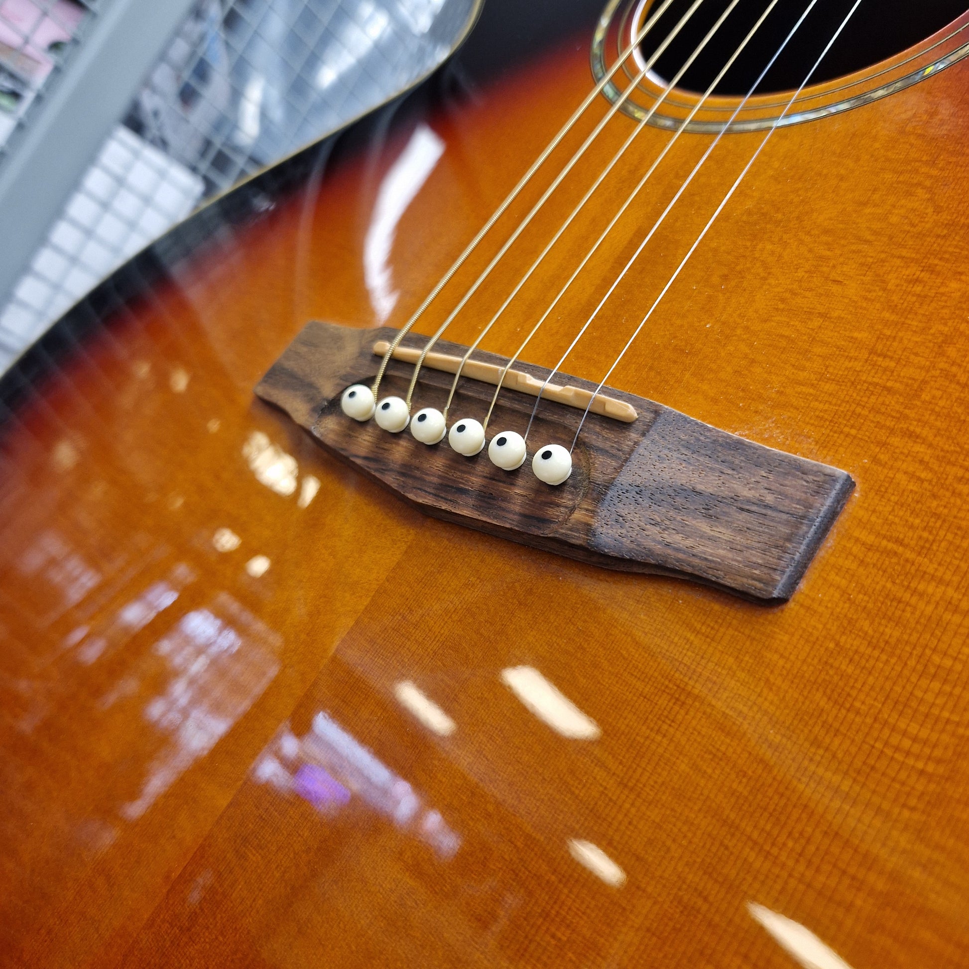 Pre-Owned Cort SFX6R Electro-Acoustic - 3-Tone Sunburst Close-up of an acoustic guitar body showing the sunburst finish, bridge, and six white oval bridge pins.