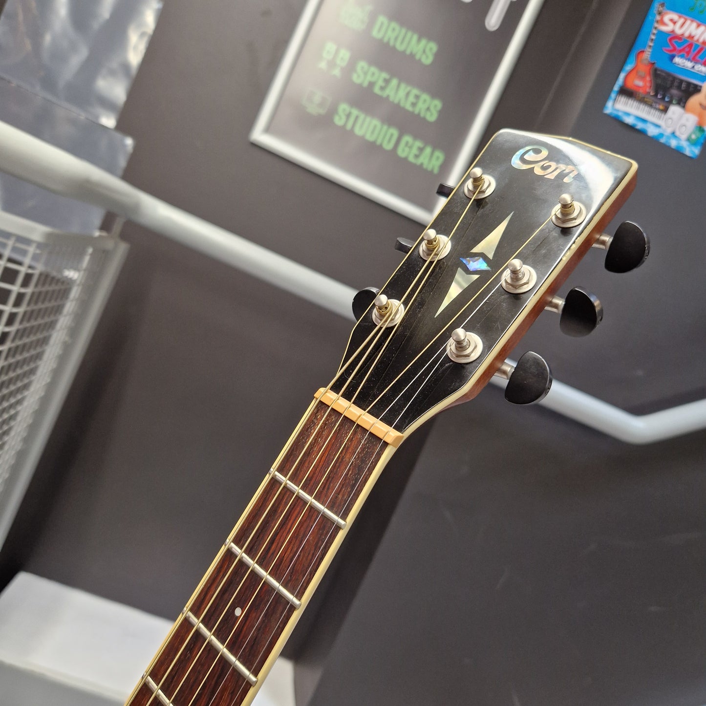 Pre-Owned Cort SFX6R Electro-Acoustic - 3-Tone Sunburst Close-up of the headstock of an acoustic guitar, showing the brand name 'Cort' in white script on a black background, with six tuning pegs and a dark brown fretboard.
