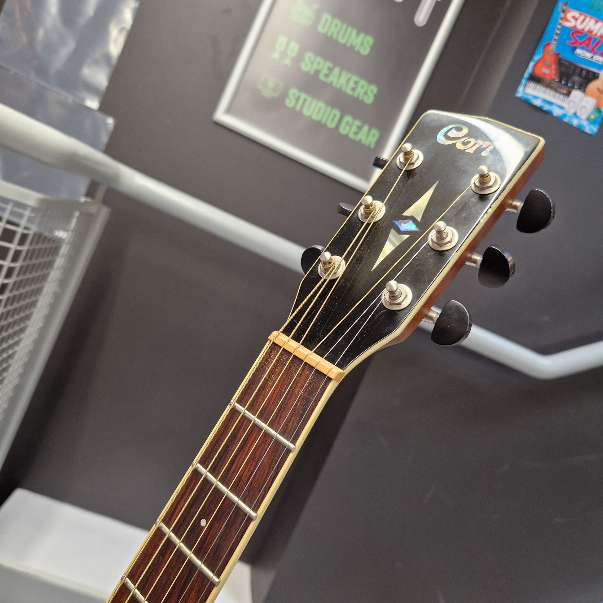 Pre-Owned Cort SFX6R Electro-Acoustic - 3-Tone Sunburst Close-up of the headstock of an acoustic guitar, showing the brand name 'Cort' in white script on a black background, with six tuning pegs and a dark brown fretboard.