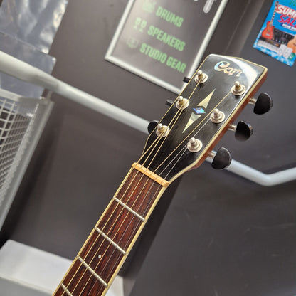 Pre-Owned Cort SFX6R Electro-Acoustic - 3-Tone Sunburst Close-up of the headstock of an acoustic guitar, showing the brand name 'Cort' in white script on a black background, with six tuning pegs and a dark brown fretboard.