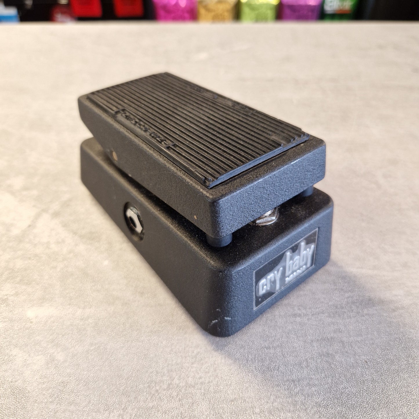 Pre-Owned Dunlop CBM95 Cry Baby Mini Wah Pedal A black guitar effects pedal with a ribbed metal footplate and a side switch, photographed on a gray textured surface. The brand name 'cry baby' is visible on the side of the unit.