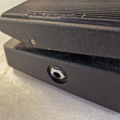 Pre-Owned Dunlop CBM95 Cry Baby Mini Wah Pedal Close-up of a black textured electronic device with a circular port, showing dust and debris on the surface.