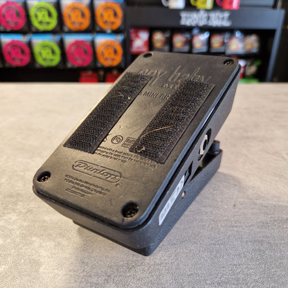 Pre-Owned Dunlop CBM95 Cry Baby Mini Wah Pedal A black Dunlop baby cradle base with velcro pads and mounting hardware, photographed on a gray tabletop with a blurred store background.