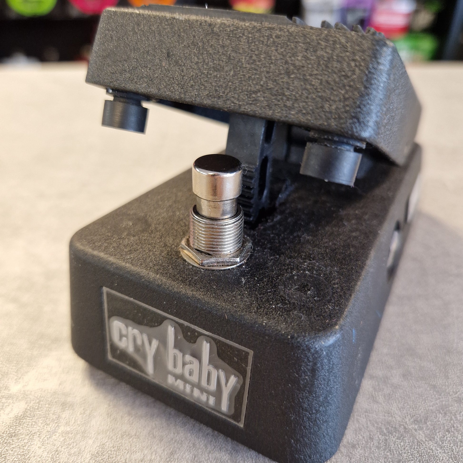 Pre-Owned Dunlop CBM95 Cry Baby Mini Wah Pedal A close-up of a black Cry Baby guitar pedal with a textured plastic body and footplate, featuring a silver metal jack adjustment on the front.