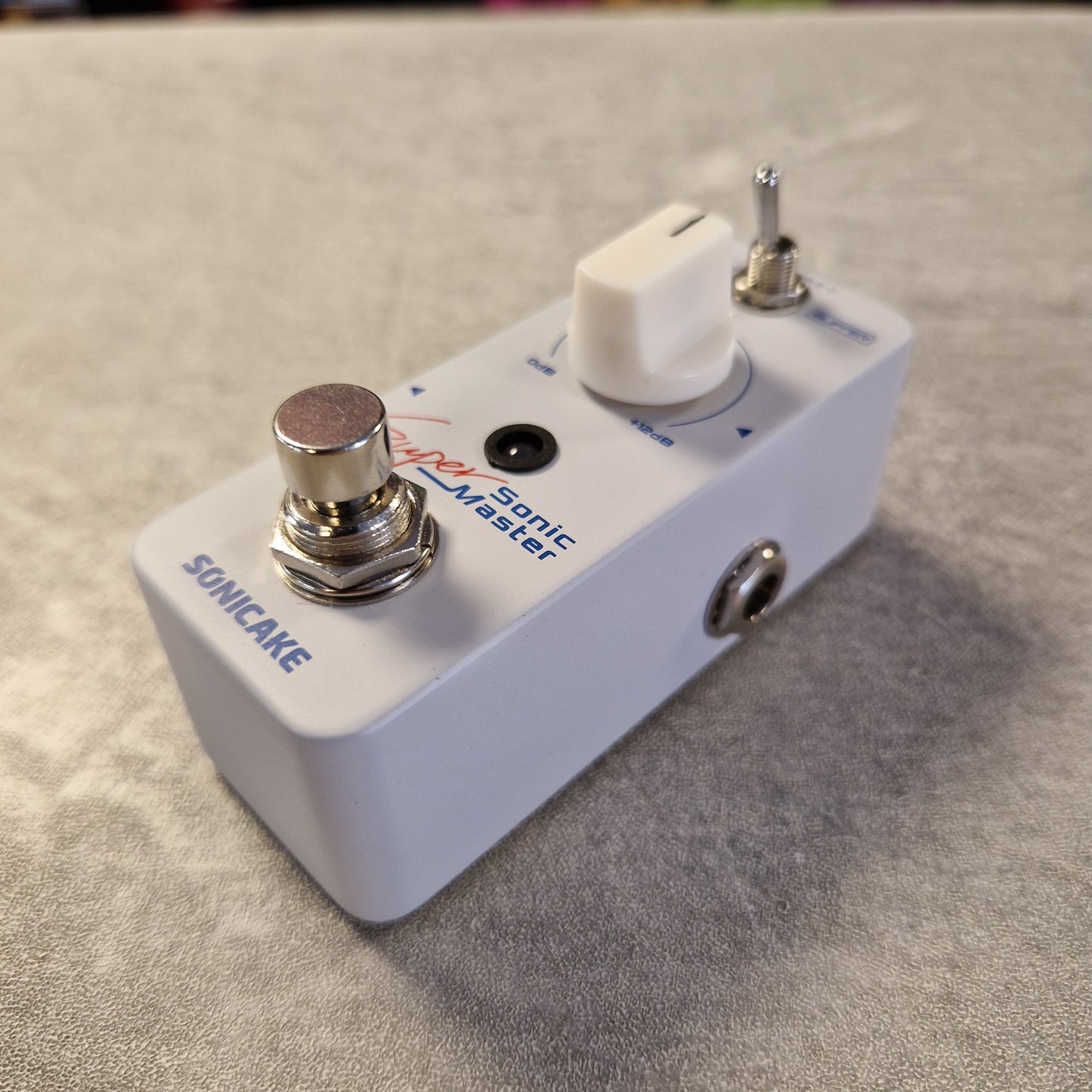 Pre-Owned Sonicake Super Sonic Master Boost Pedal A white Sonicake Somatic Master guitar effects pedal with chrome metal controls, photographed on a textured gray surface.