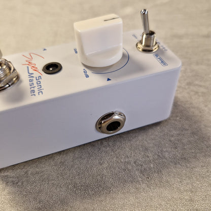 Pre-Owned Sonicake Super Sonic Master Boost Pedal A close-up of a white Sonic Master Super Master guitar effects pedal, showing the white volume knob, silver toggle switch, and metal jack connectors on a textured gray surface.