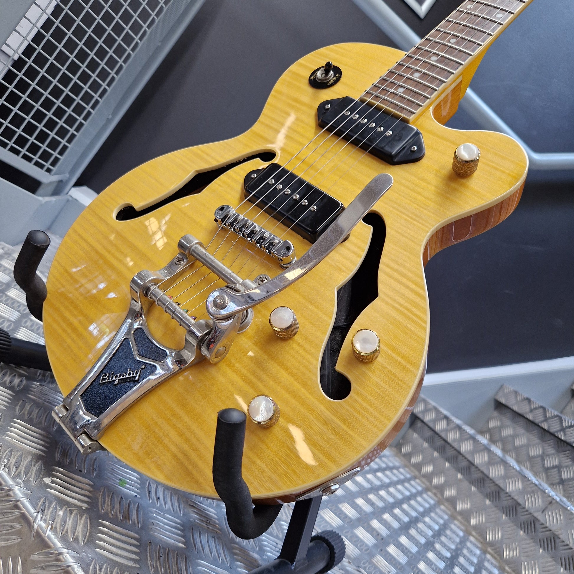 Pre-Owned Epiphone Wildkat Hollow-Body Electric - Natural Amber A close-up of a yellow-finish double-cutaway electric guitar on a stand, showing a silver Leslie speaker mount, black pickups, and gold-toned control knobs.