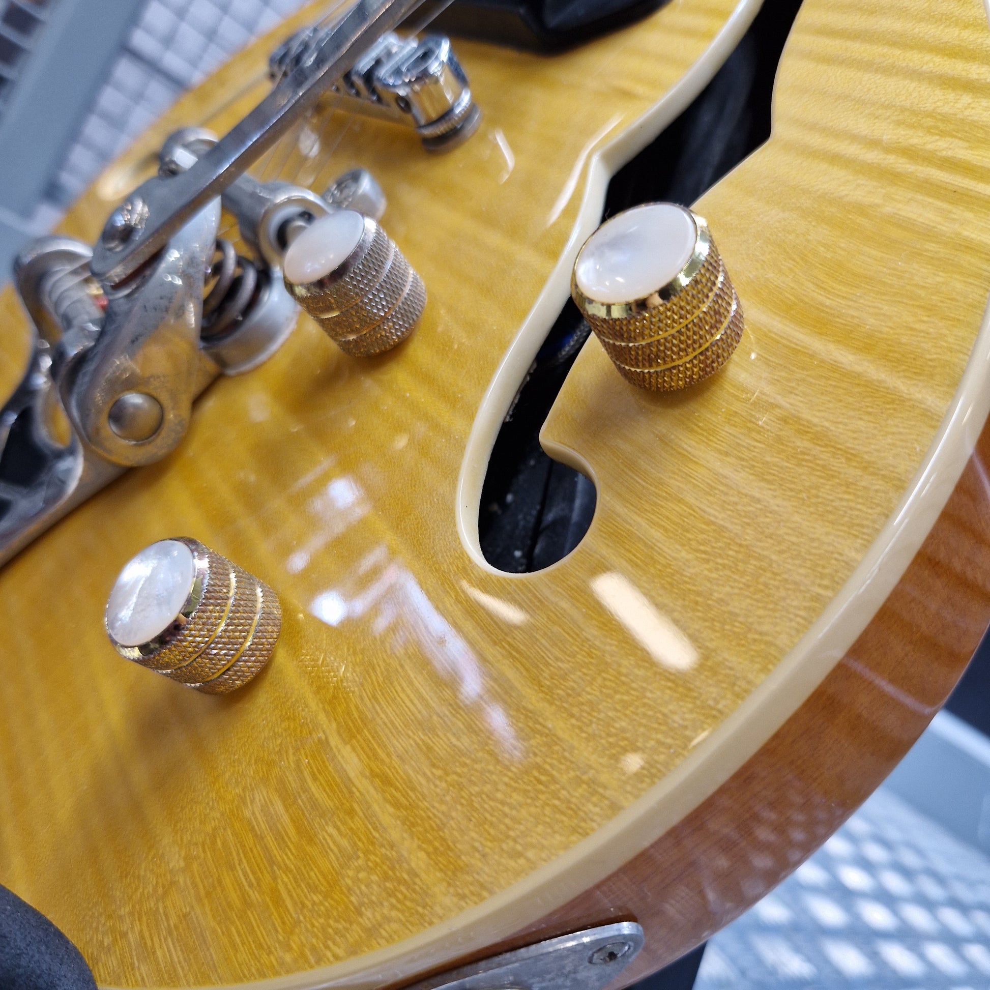 Pre-Owned Epiphone Wildkat Hollow-Body Electric - Natural Amber Close-up of a glossy sunburst electric guitar body showing a flamed maple wood finish, gold-toned hardware, and control knobs.