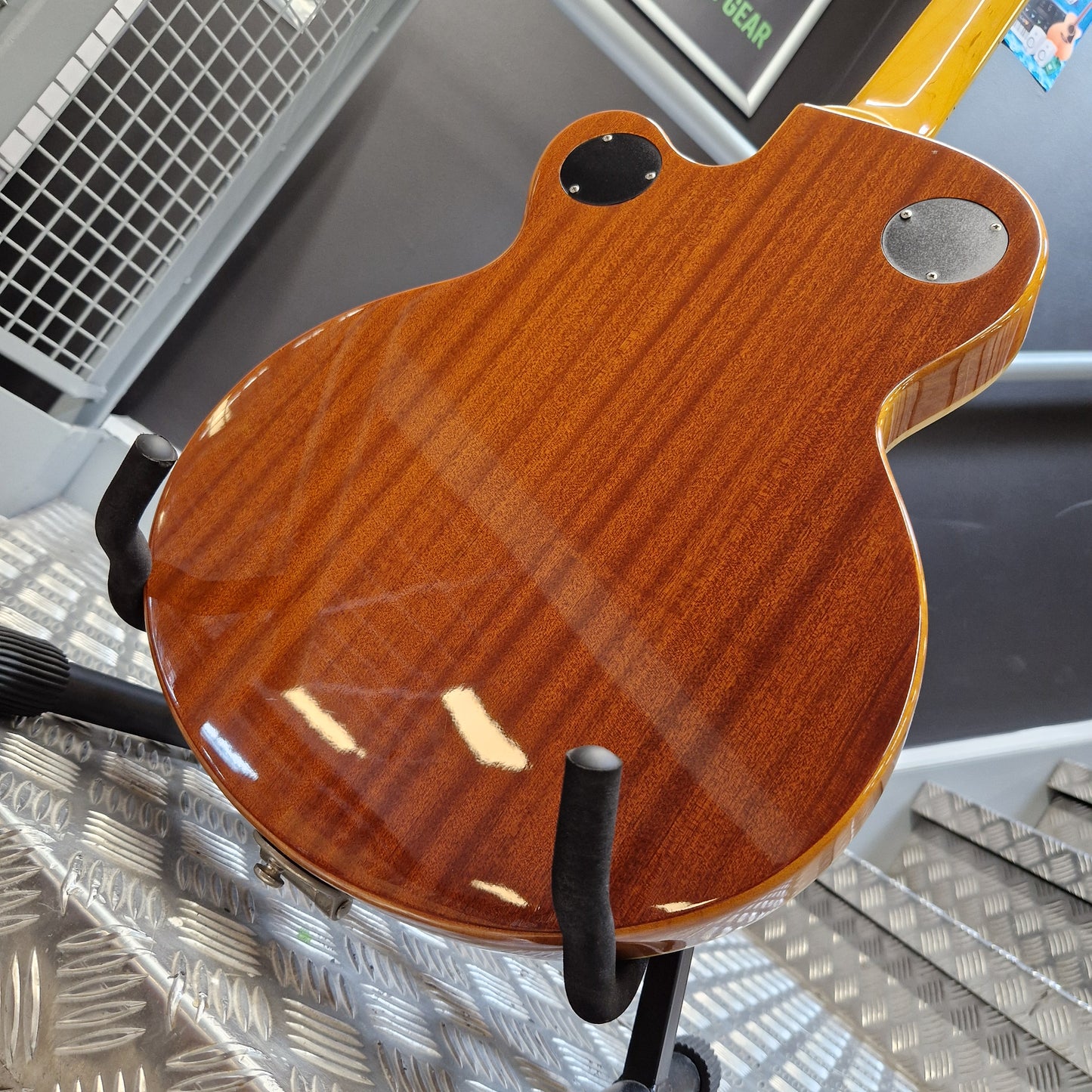 Pre-Owned Epiphone Wildkat Hollow-Body Electric - Natural Amber Close-up of the back of a glossy electric guitar body with a warm reddish-brown wood finish, mounted on a stand in a workshop setting.