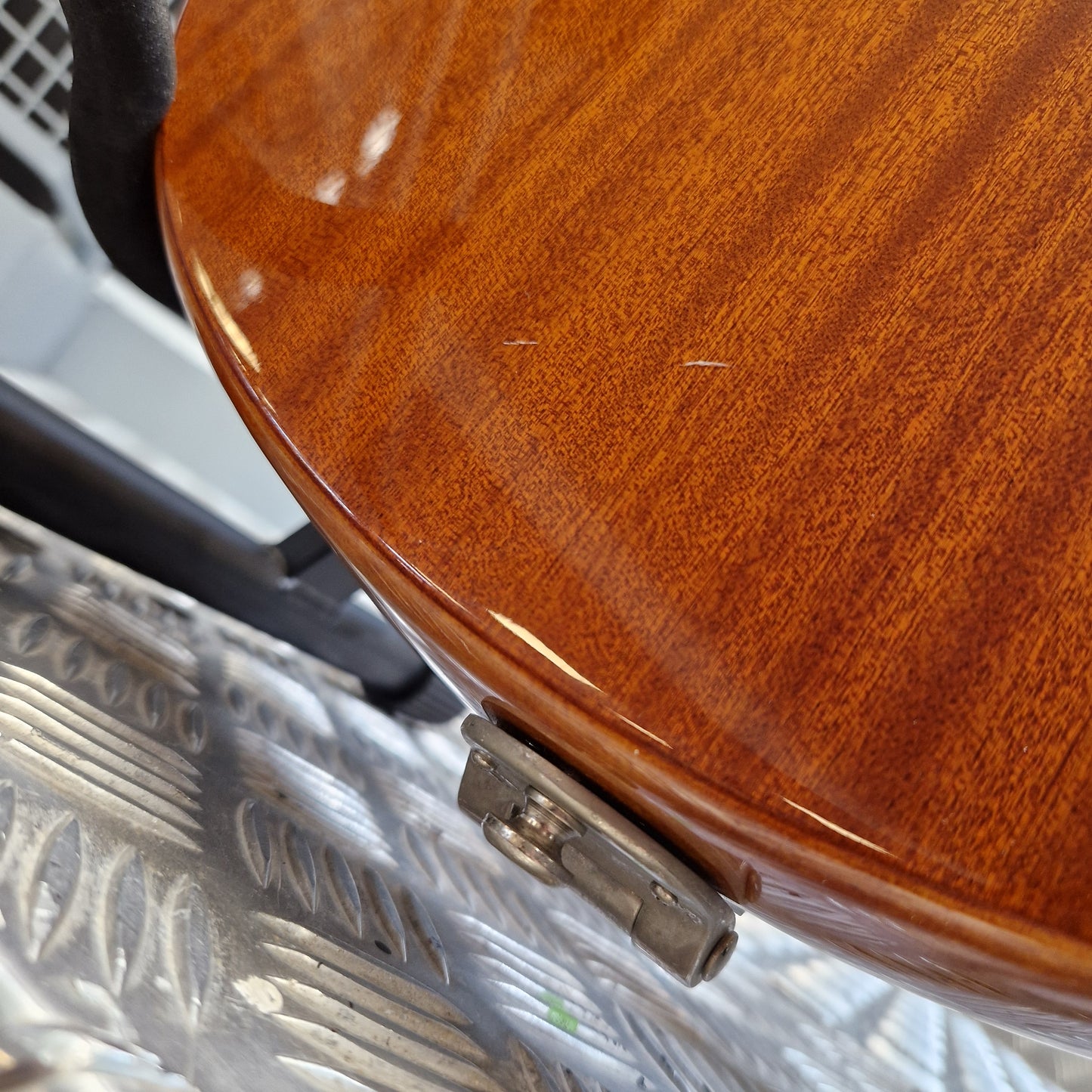 Pre-Owned Epiphone Wildkat Hollow-Body Electric - Natural Amber Close-up of the glossy reddish-brown wood body of an electric guitar resting on a silver diamond plate floor.