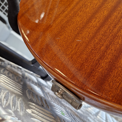 Pre-Owned Epiphone Wildkat Hollow-Body Electric - Natural Amber Close-up of the glossy reddish-brown wood body of an electric guitar resting on a silver diamond plate floor.