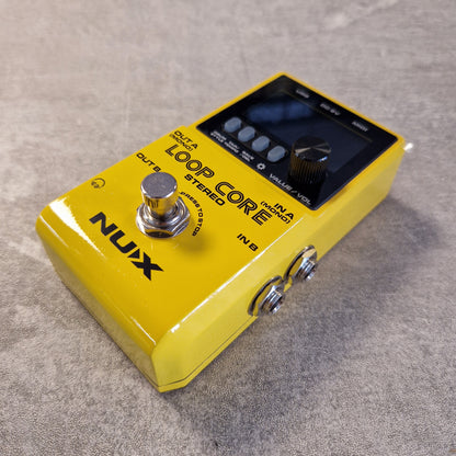 Pre-Owned Nux Loop Core Stereo Looper Pedal A yellow Nux Loop Core guitar effects pedal with a digital display screen, silver footswitch, and metal input/output jacks, resting on a textured gray surface.