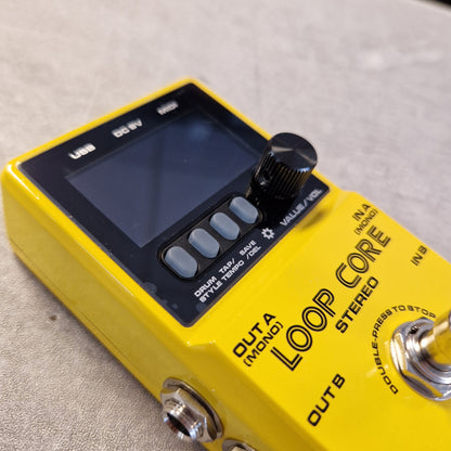 Pre-Owned Nux Loop Core Stereo Looper Pedal A close-up of a yellow Boss Loop Core guitar effects pedal with a black display screen, control buttons, and footswitches on a textured gray surface.