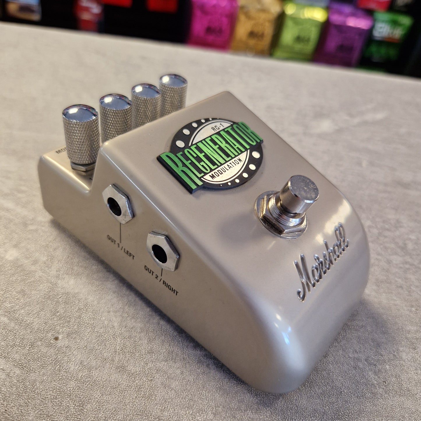 Pre-Owned Marshall RG1 Regenerator Modulation Pedal A Marshall Greenwald Overdrive guitar pedal with a metallic silver body, featuring five silver knobs, a silver footswitch, and a green and black Greenwald logo on top, set on a gray textured surface.