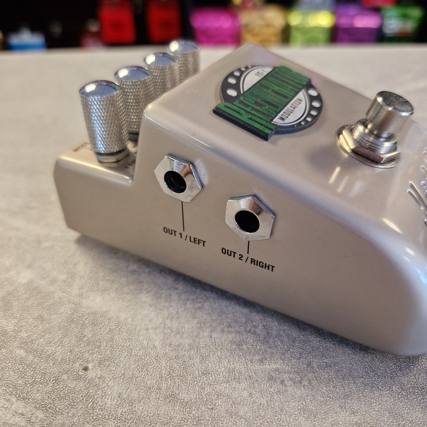 Pre-Owned Marshall RG1 Regenerator Modulation Pedal A close-up of a beige guitar effects pedal with silver knobs, two output jacks labeled OUT 1/LEFT and OUT 2/RIGHT, and a green-and-black label on top, resting on a gray textured surface.