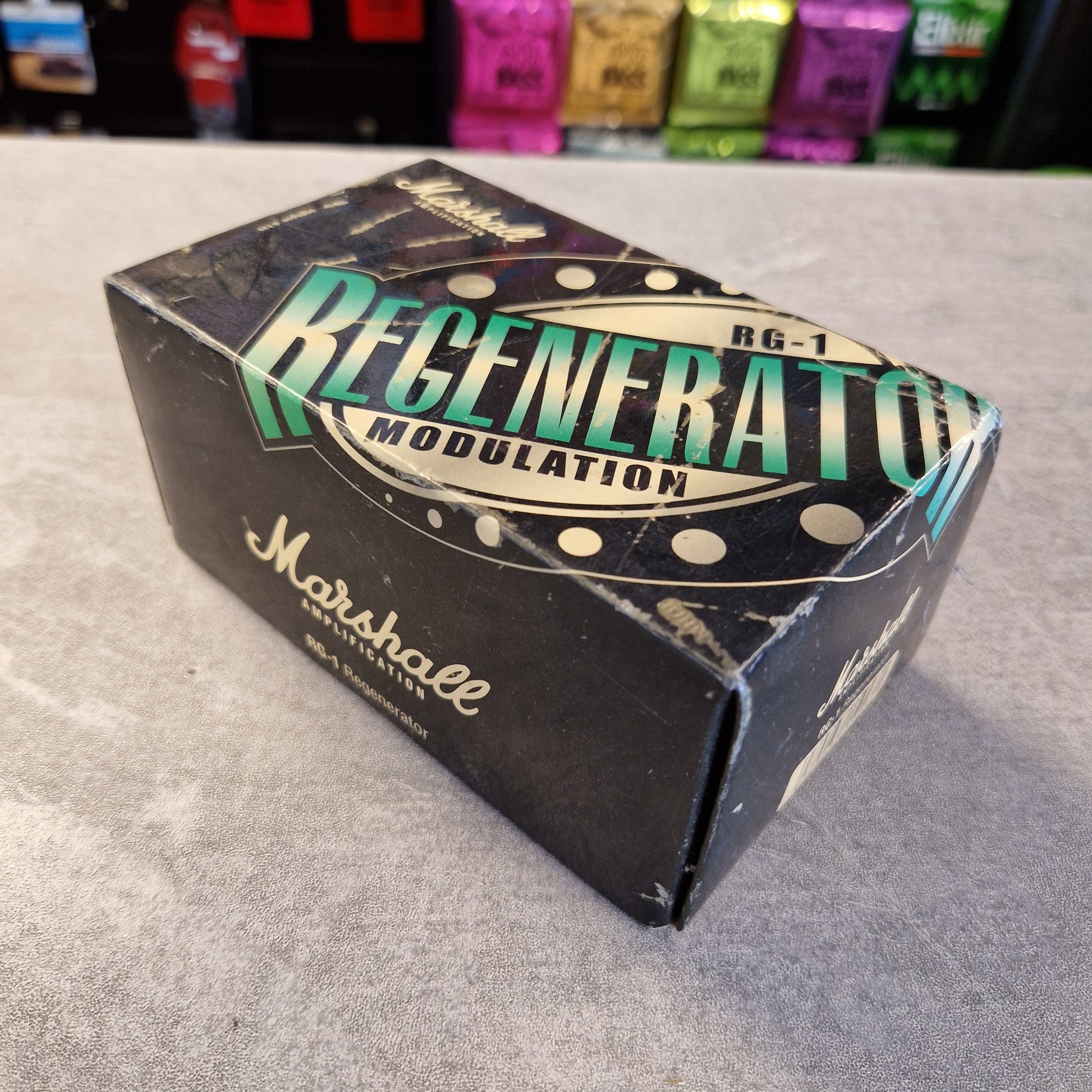 Pre-Owned Marshall RG1 Regenerator Modulation Pedal A vintage Marshall RG-1 Regenerator Modulation amplifier box, showing the black original packaging with green and gold lettering, placed on a gray textured surface.
