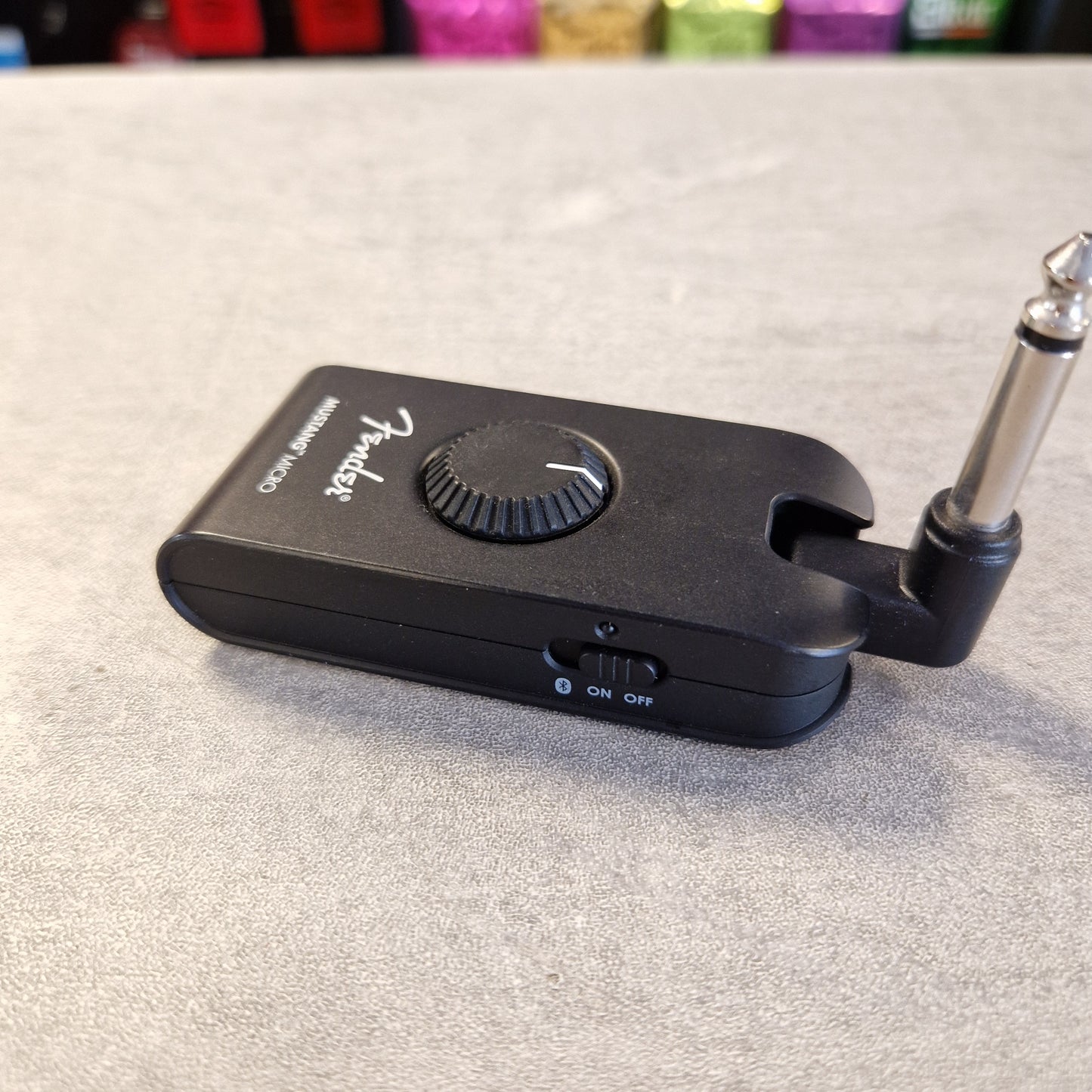 Pre-Owned Fender Mustang Micro Headphone Guitar Amplifier A black Fender speaker emulator/clipper device with a 1/4-inch jack plug attached, resting on a gray textured surface.