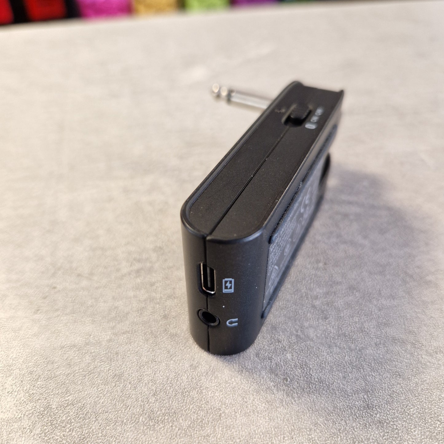 Pre-Owned Fender Mustang Micro Headphone Guitar Amplifier A black electronic device, likely a portable audio receiver or mixer module, shown from an angle on a textured gray surface.