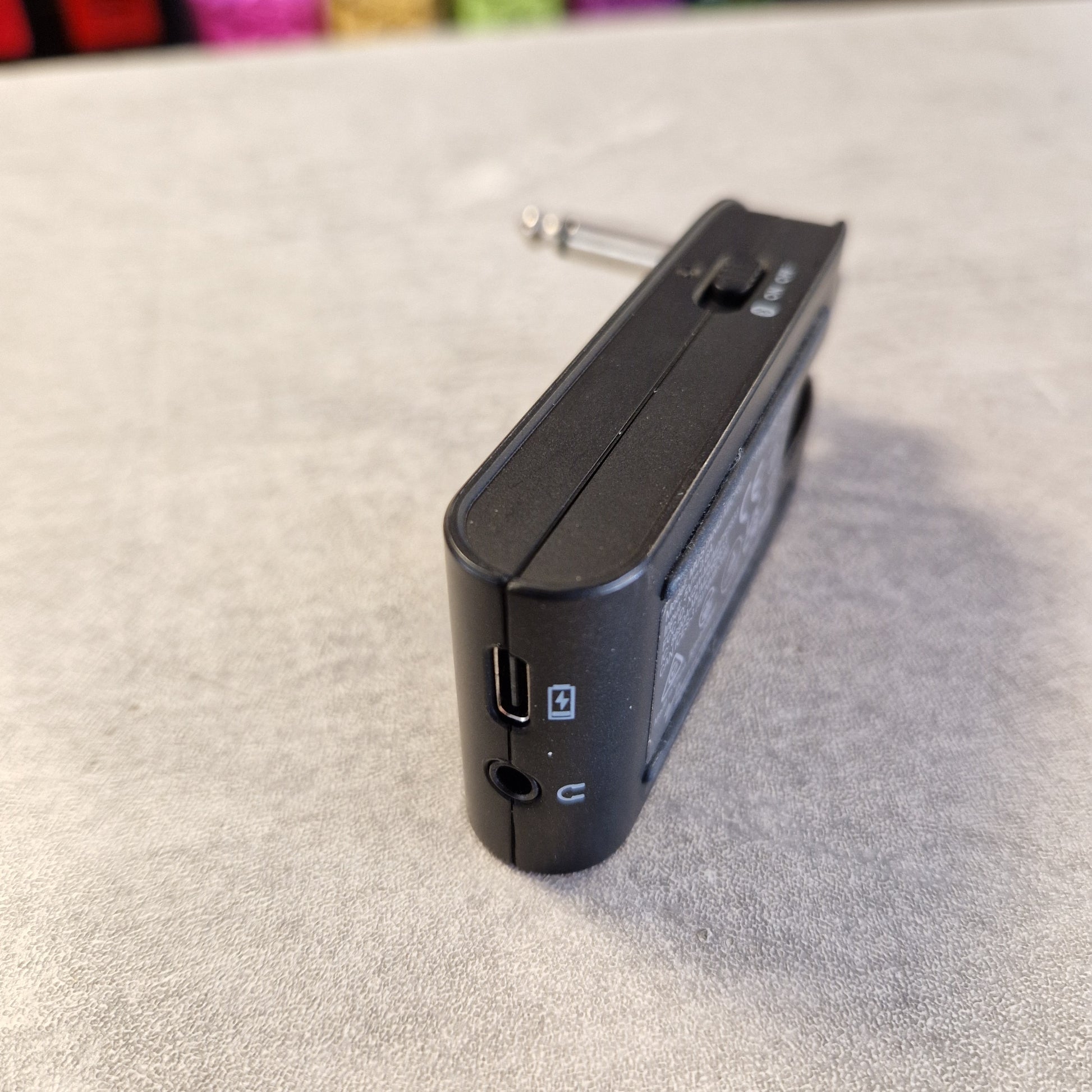 Pre-Owned Fender Mustang Micro Headphone Guitar Amplifier A black electronic device, likely a portable audio receiver or mixer module, shown from an angle on a textured gray surface.