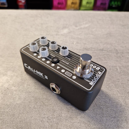 Pre-Owned Mooer 008 Cali-Mk3 Dual Channel Preamp Pedal A Call of Mk III Megaphone guitar effect pedal with a black metal body, white and silver knobs, and a silver footswitch, resting on a gray textured surface.