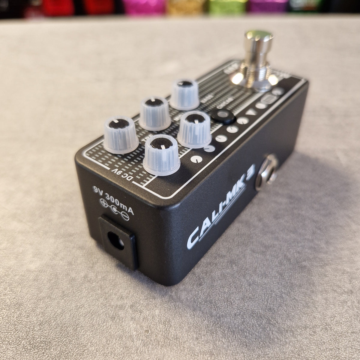 Pre-Owned Mooer 008 Cali-Mk3 Dual Channel Preamp Pedal A black Calhoun 3 guitar effects pedal with white and silver knobs, a footswitch, and white printed markings, resting on a gray textured surface.